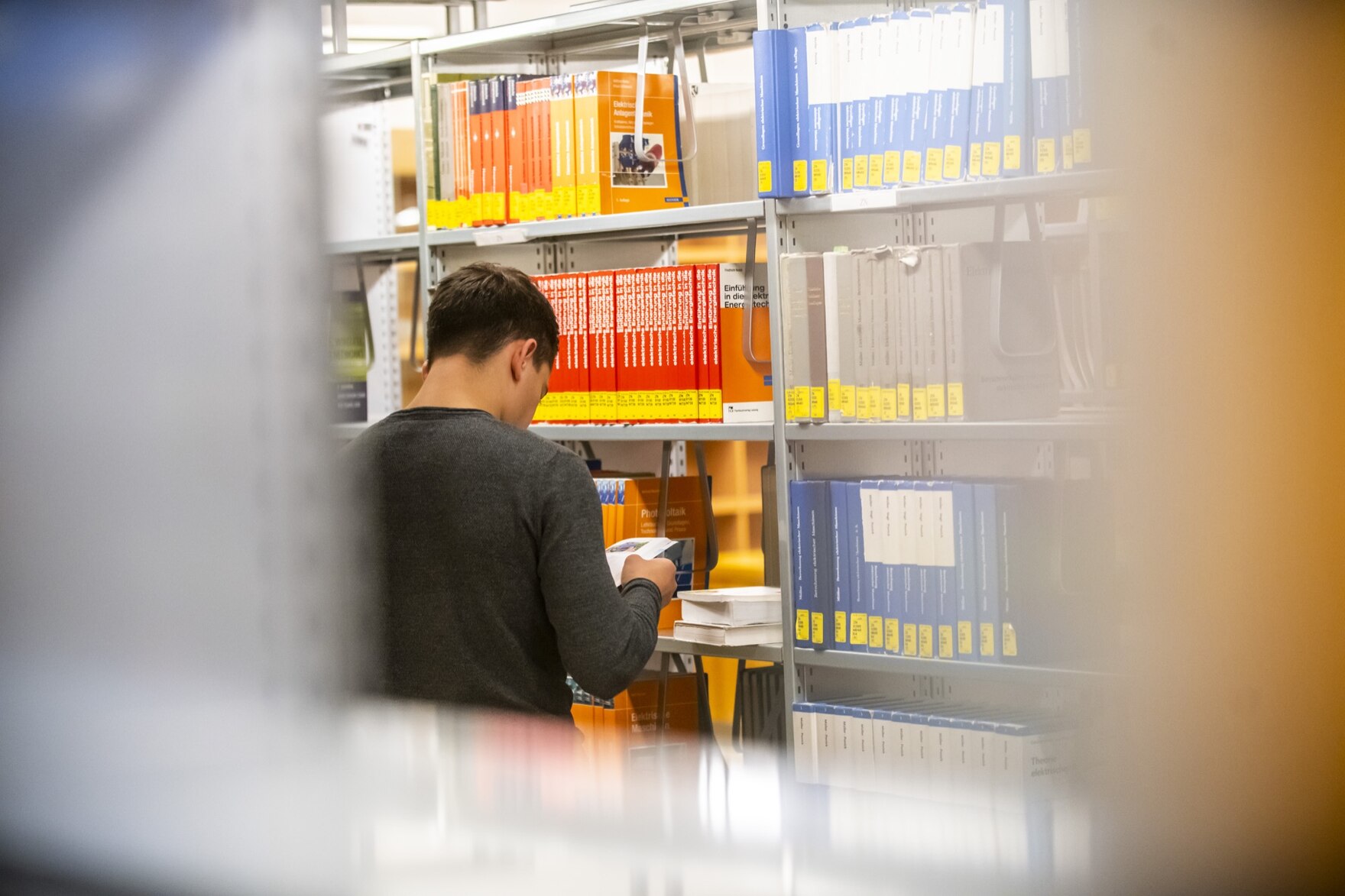 Junger Mann von hinten, der vor einem Bücherregal steht. Die Ränder sind verschwommen