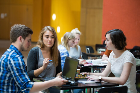 Drei Studierende arbeiten gemeinsam mit Laptop und Unterlagen an einem Tisch. 